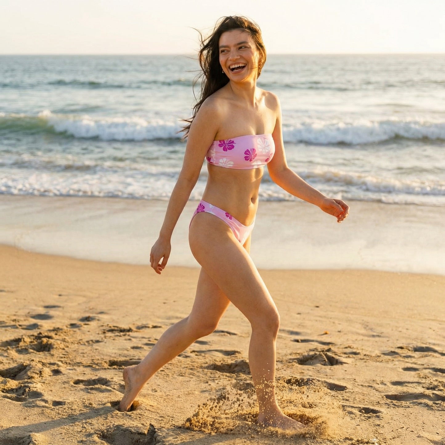 Woman in a pink hibiscus bikini walking on a beach with ocean waves in the background