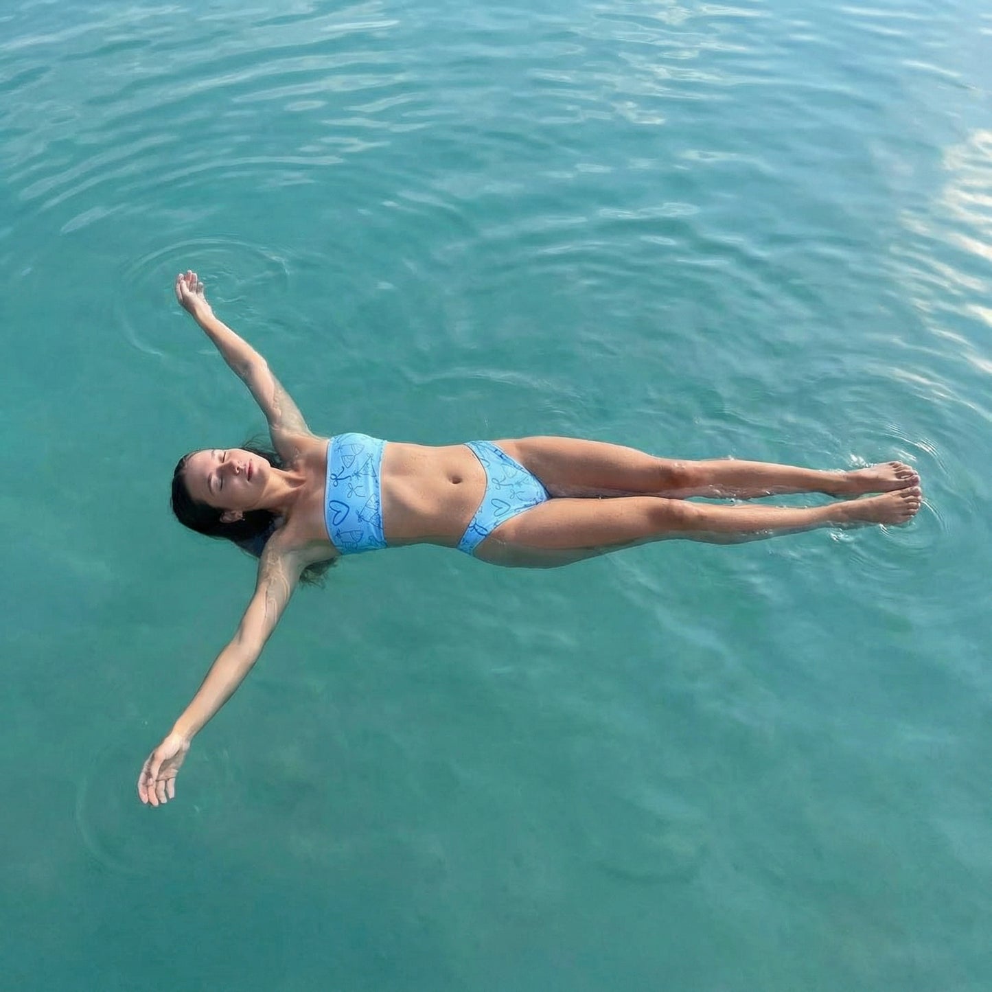 Woman wearing the Vibewear 'Blue Crush' bandeau bikini set, which features a vibrant blue abstract pattern, a strapless top, and flattering high-leg bottoms.