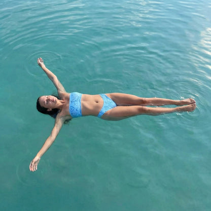 Woman wearing the Vibewear 'Blue Crush' bandeau bikini set, which features a vibrant blue abstract pattern, a strapless top, and flattering high-leg bottoms.