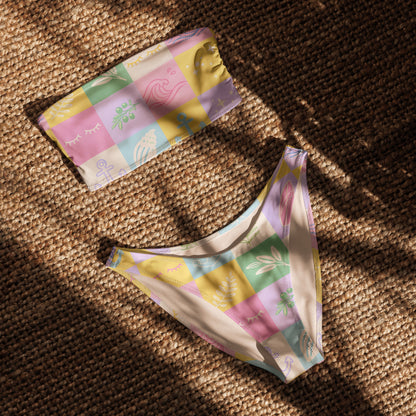 Recycled bandeau bikini with pastel patchwork pattern laid flat on woven mat
