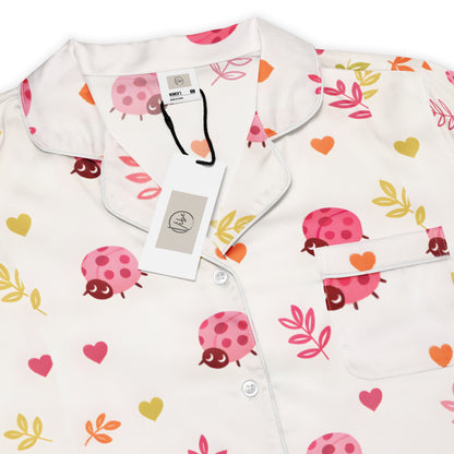 Woman wearing the Vibewear 'Ladybird Daydream' long sleeve satin pajama top, showing the cute red ladybug pattern and classic button-front style.